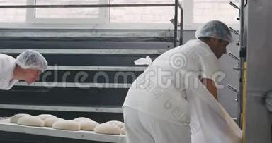 面包业的两名工人把生面包装进烤箱机进行烘烤，他们穿着特殊的白色衣服