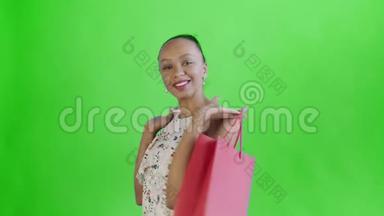 一位非洲裔美国妇女在摄影棚里，双手拿着购物袋，在绿色背景<strong>下摆</strong>姿势。幸福女人抱