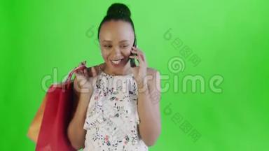 年轻漂亮的非洲人在录音室里用手机拿着绿色背景的购物袋。带花的白色连衣裙