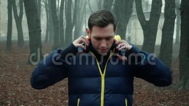 男运动员在城市公园里戴上无线耳机，寒冷的雾天早晨
