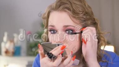 眼部化妆。 女孩看着一面小手镜子。 在睫毛上涂上黑色油漆。