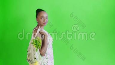 漂亮的美国黑人妇女手里拿着可重复使用的网状编织购物袋，里面有<strong>水果</strong>、<strong>蔬菜</strong>和<strong>蔬菜</strong>