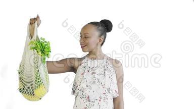 漂亮的美国黑人妇女手里拿着可重复使用的网状编织购物袋，里面有水果、蔬菜和蔬菜