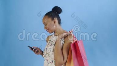 在<strong>录音</strong>室里，一位拿着购物袋的非裔美国妇女正在用蓝色背景的智能手机交谈。白色连衣裙