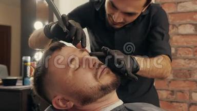 在男式沙龙里，用直剃须刀将理发师刮胡子贴在脸上。 脸上留着剃须刀的头发