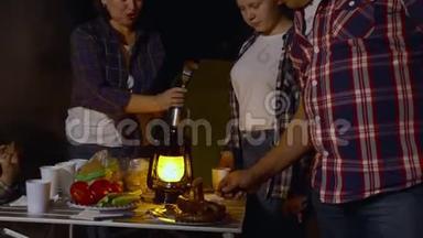 旅游家庭在营地的森林徒步旅行中晚餐吃烧烤香肠。 妈妈，爸爸，儿子和女儿吃油炸食品
