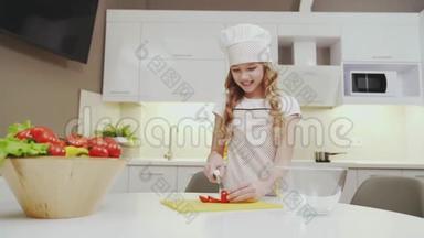 穿着厨房围裙和帽子的可爱女孩切番茄做沙拉