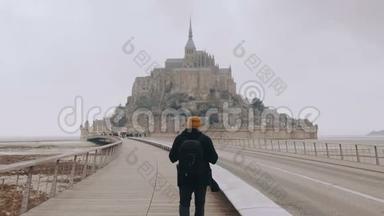 镜头跟随快乐兴奋的旅游者，背着背包，在诺曼底慢步走向史诗般的圣米歇尔山城堡。