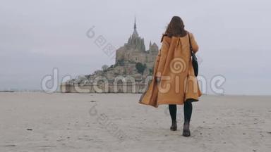 后景放大时尚旅游妇女慢慢走在海沙上史诗圣米歇尔城堡慢动作。