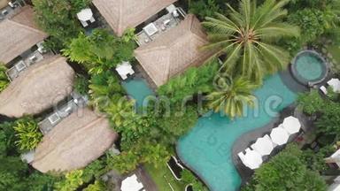 带草屋顶别墅和热带丛林和棕榈树的游泳池的豪华酒店的无人机鸟瞰。 豪华别墅