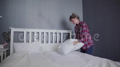 女人在卧室里打扫她的床，漂亮的女人摆好床，整理她的枕头和垫子