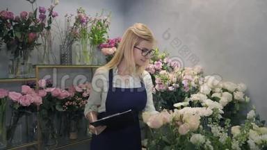 鲜花店，花卉精品店女小企业主的肖像，微笑着在温室里检查鲜花