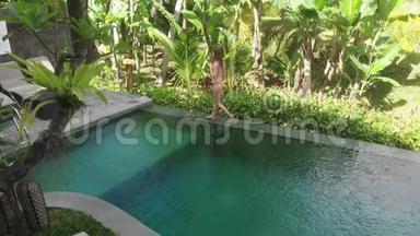 带热带花园的别墅无限游泳池鸟瞰图。女人走在池边欣赏丛林风光