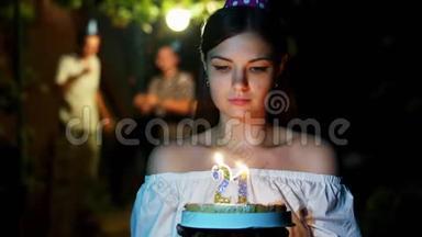 <strong>美女</strong>拿着生日蛋糕和蜡烛站着许愿，朋友们在后台<strong>跳舞</strong>