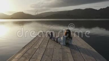 一位从背后看到长发的年轻女子在夕阳下看湖，她躺在一个古老的<strong>木墩</strong>上