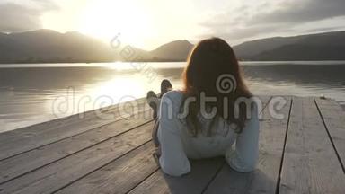 一位从背后看到长发的年轻女子在夕阳下看湖，她躺在一个古老的<strong>木墩</strong>上
