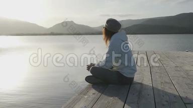站在一个古老的木墩上，一位从侧面看到长发的年轻女子在日落时看着湖面
