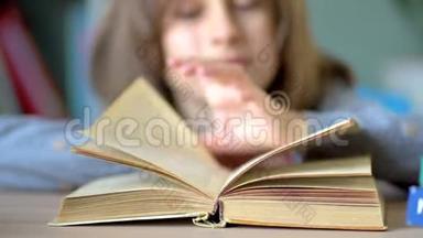 最喜欢的爱好是读书。 桌子上有一本打开的书。 一个年轻的女学生读起来很感兴趣。 关闭视野。