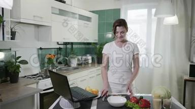 迷人的微笑女孩在烹饪时玩得很开心，并观看了一个关于健康饮食的流行博客的食谱视频。