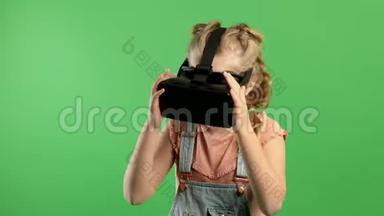 慢动作微笑的小女孩玩虚拟现实眼镜，女孩站在孤立的绿色背景。 概念