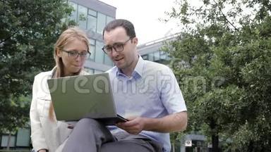 一起上网冲浪。 商务同事一起坐在长凳上看着笔记本电脑。