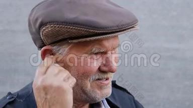 戴着帽子的霍利退休男子正双人敲击无线耳机打开音乐。 穿蓝色夹克的养老金领取者正在享受