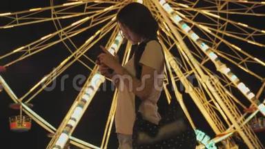 快乐美女亚洲女人看智能手机聊天与朋友在游乐园背景与摩天轮骑