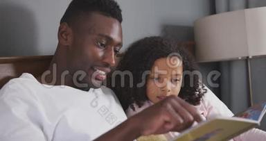 非裔美国父亲在床上给女儿读故事