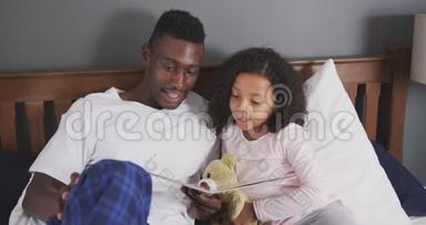 非裔美国父亲在床上给女儿读故事