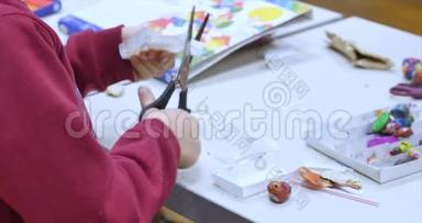 艺术工作室里的年轻艺术家或男孩坐在一张桌子旁，用纸剪刀剪一个图形。 <strong>学习过程</strong>或