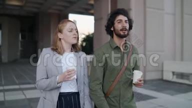 年轻的职业男人和女人从办公楼出来，拿着外卖的咖啡杯微笑着和每个人交谈