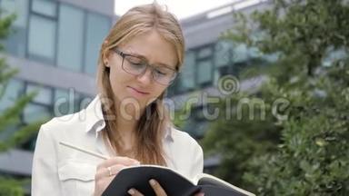 戴着眼镜的漂亮沉思的年轻学生拿着一本笔记本和一支铅笔，<strong>看</strong>着<strong>远方</strong>，思考着。