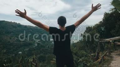 一位年轻的旅行者高高举起双手，站在山顶上