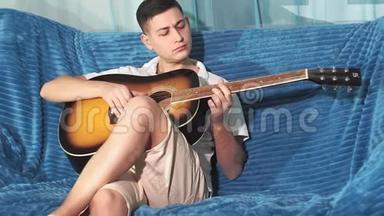 年轻人坐在沙发上弹吉他。 击中摄像机。 学弹吉他