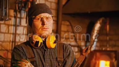 <strong>锻造</strong>工业-一个戴眼镜和耳机的铁匠拿着钳子，看着相机