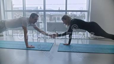 现代<strong>健身房</strong>-男人和女人在<strong>健身房</strong>训练-在瑜伽垫上拿着木板