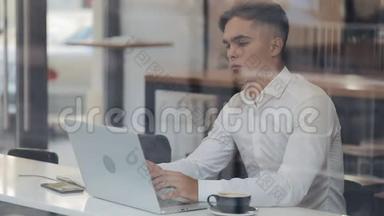 年轻有魅力的商人靠在笔记本电脑上完成办公室工作，工作完成后感到轻松。 他在伸展