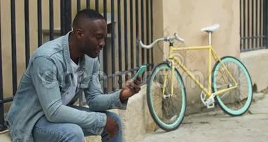 微笑非裔美国人年轻人坐在自行车旁时，通过他的智能手机打视频电话，挥手和微笑