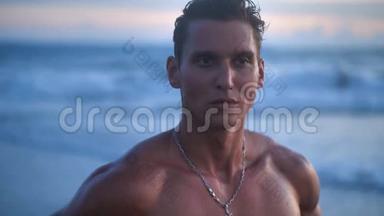 英俊的运动员，训练有素的肌肉运动员的肖像，在美丽的日落时在海滩上摆姿势