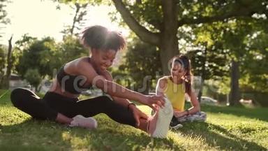 一位身穿运动服的年轻女士微笑着，和她的朋友坐在公园里的草地上，伸展着双腿