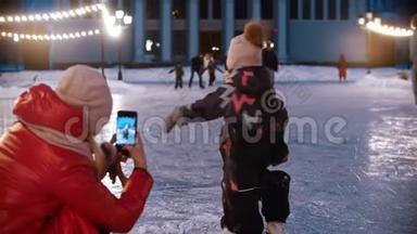 两个小孩在溜冰场上跳舞-他们的母亲用电话<strong>摄影机</strong>拍摄他们