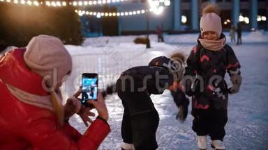 两个小孩在冰场上-他们的母亲用电话<strong>摄影机</strong>拍摄他们