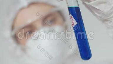 一位年轻的女科学家检查一支蓝色药物的试管。 一个戴防护面罩和眼镜的女孩在检查一项测试