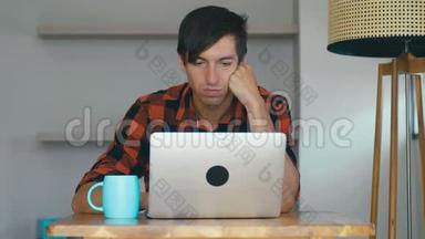 年轻的商人坐在家里的办公桌前用笔记本电脑。 自由职业者在家里和