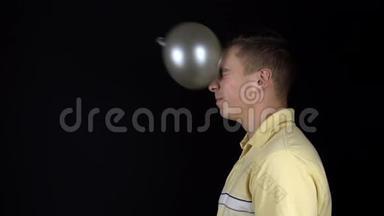 那人脸上有一个气球。 一个年轻人站在黑色的背景上。 一个装满水的气球