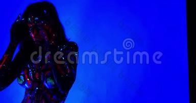 一位年轻女子在紫外光照射下跳舞摆姿势，身上散发出绚丽多彩的身体艺术