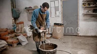 混凝土行业-青年工人用手搅拌机将混凝土从水泥水和玻璃碎片中搅拌出来