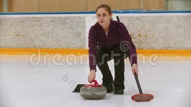 冰场上的弯曲训练-一个年轻的女人用刷子把石头推到冰场上