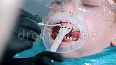 一个戴<strong>防</strong>护<strong>眼镜</strong>的小男孩在现代牙科中进行牙齿清洁治疗-用一个