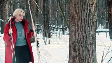 一个年轻的金发女子穿着红色<strong>羽绒服</strong>，把她的滑雪板放在森林里的树旁